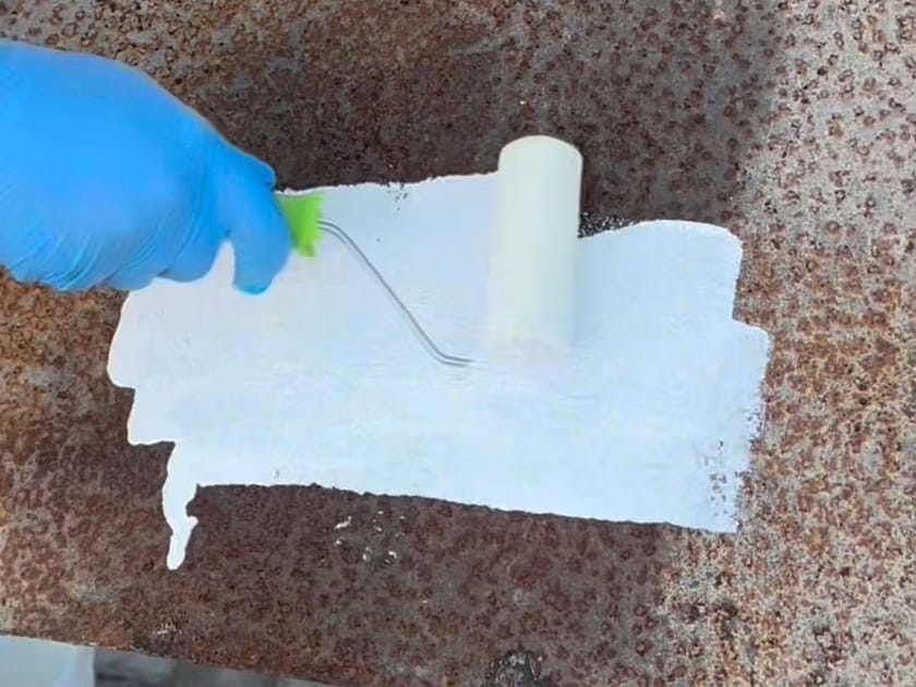 Rolo passando tinta branca direto sobre uma chapa metálica enferrujada